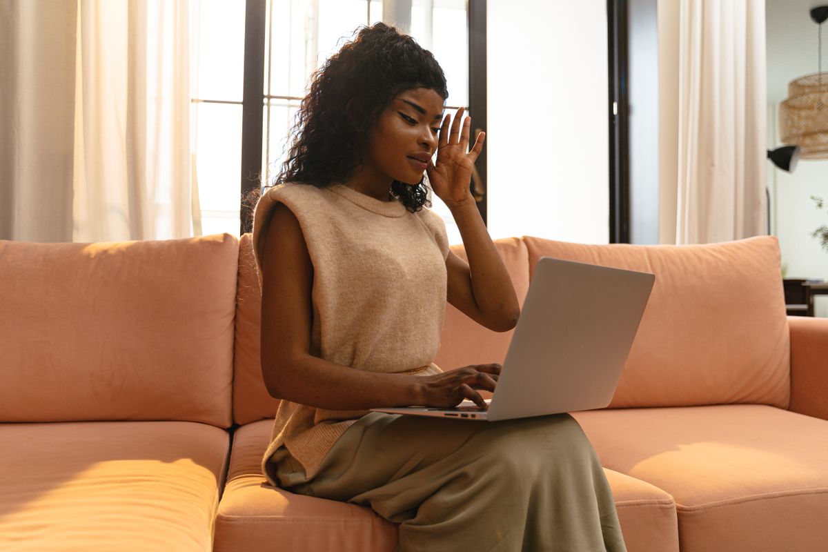 A woman browses deals on her laptop in a sunlit living room