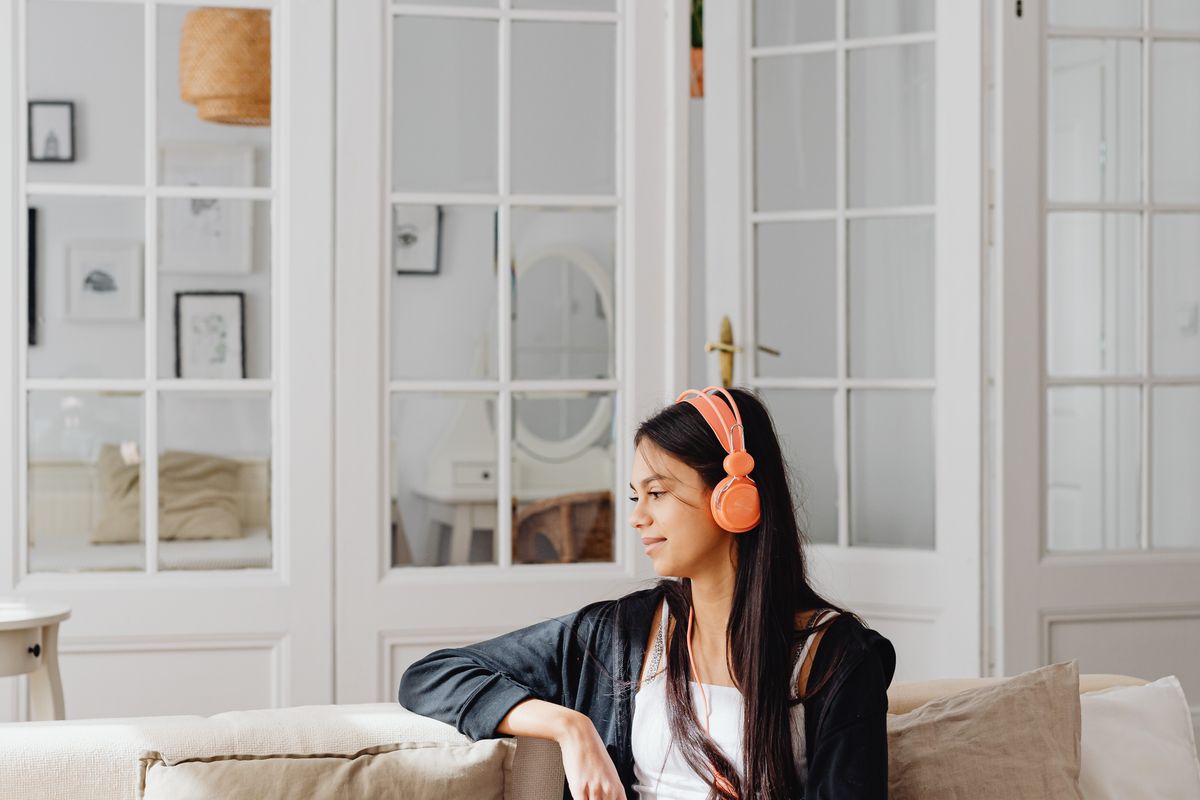A woman relaxes on her sofa listening to music with headphones