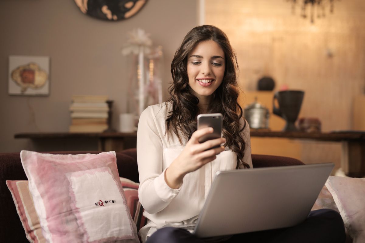A woman relaxes on her couch with her phone and laptop